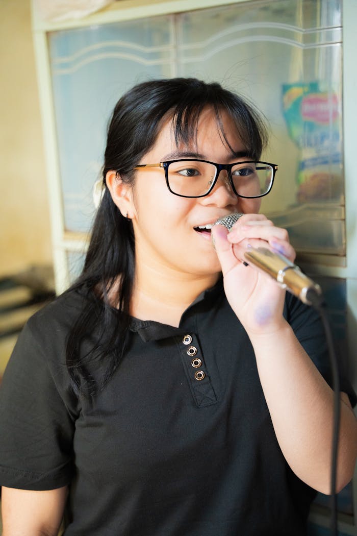 creative-approach-img A young woman enjoys singing with a microphone indoors, showcasing a casual and joyful moment.