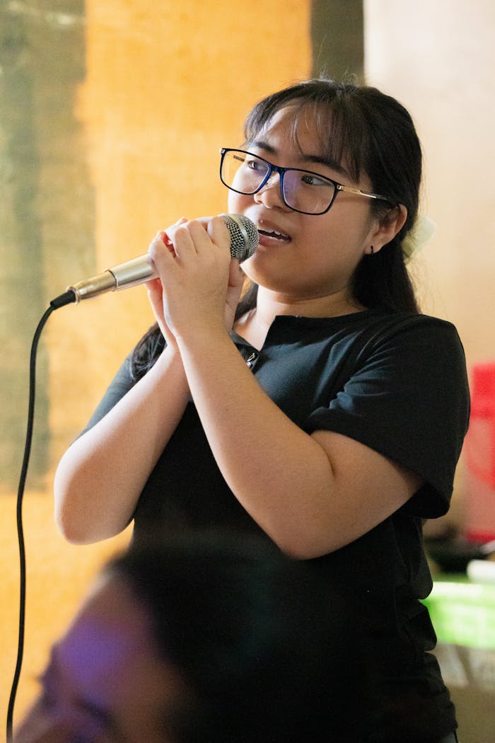 our-mission Young woman passionately singing karaoke with microphone indoors.