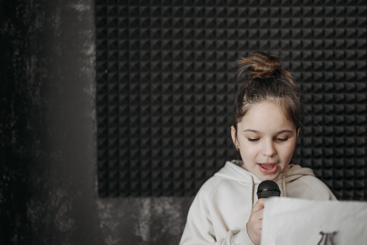 A young girl singing into a microphone in a soundproof recording studio.